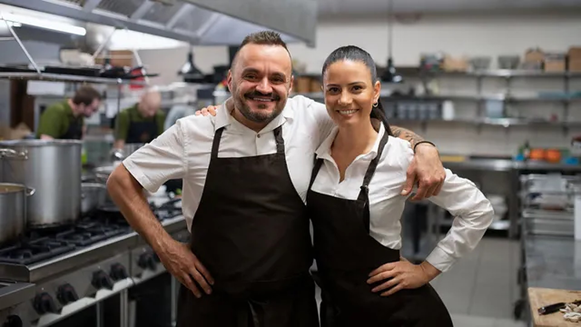 Koch und Köchin in Schürzen lächeln in einer Restaurantküche