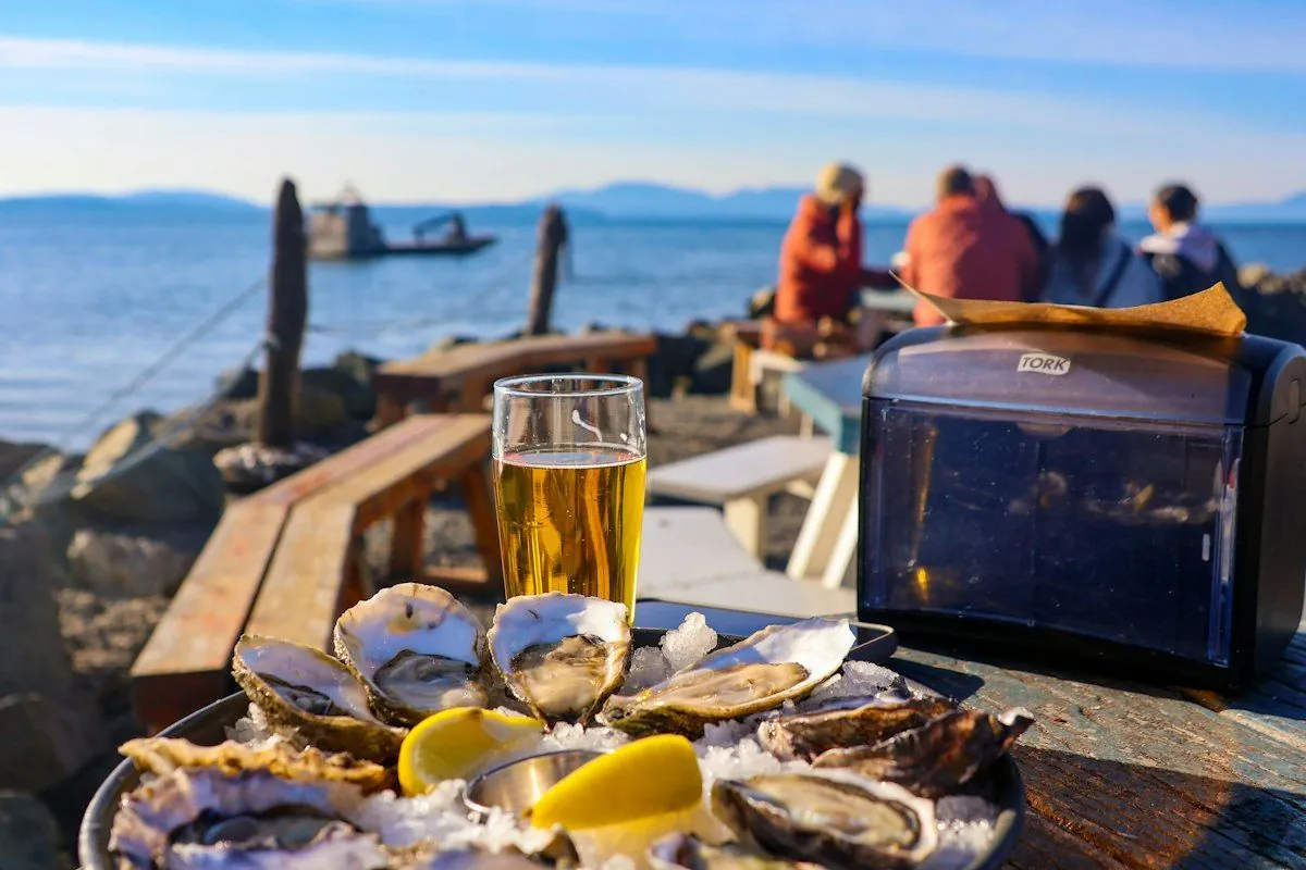 Bier und Austern am Meer, im Hintergrund sitzen Menschen am Wasser